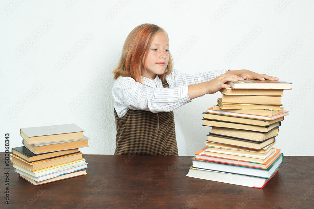 A teenage girl takes books from a stack of books on the table. A teenage girl takes books from a stack of books on the table.