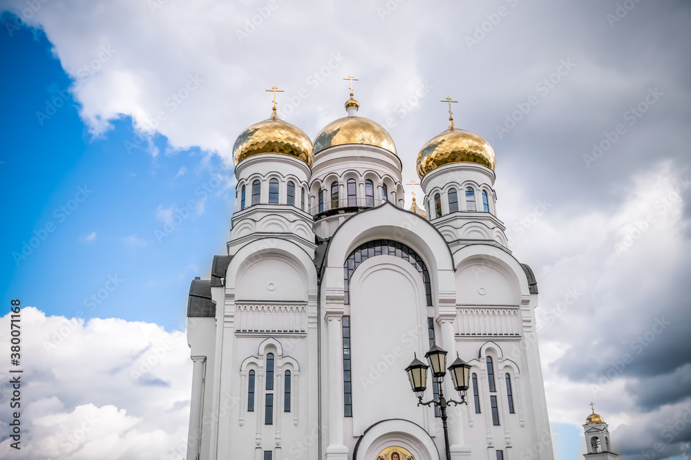 Golden domes, cupolas with Eastern Orthodox crosses on a white Church against a blue sky with clouds