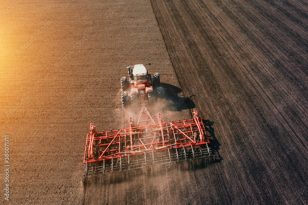 Fototapeta Tractor cultivating or plowing agriculture field in sunset light, aerial view.