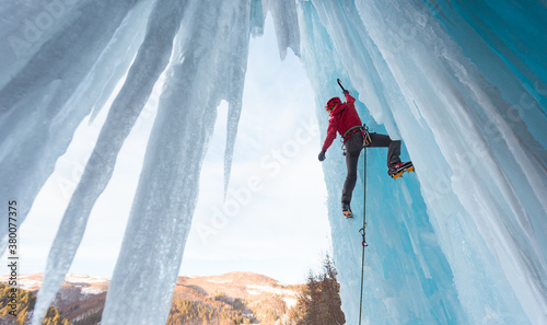Female ice climber admiring hanging on ice axe