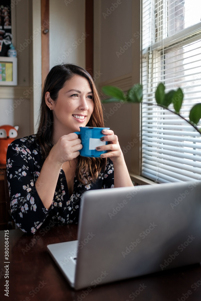 Beautiful woman holding a cup of coffee working on her laptop at Beautiful woman holding a cup of coffee working on her laptop at