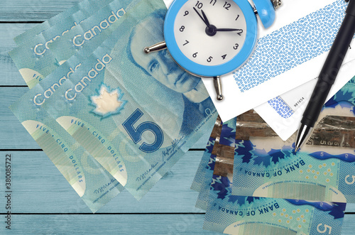 5 Canadian dollars bills and alarm clock with pen and envelopes. Tax season concept, payment deadline for credit or loan. Financial operations using postal service photo