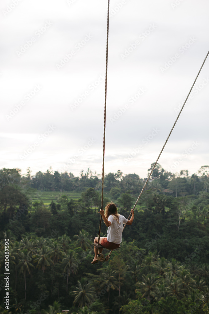 Woman swinging over tropical valley on rope swing Woman swinging over tropical valley on rope swing