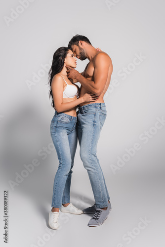 muscular man standing and touching seductive woman in bra on grey