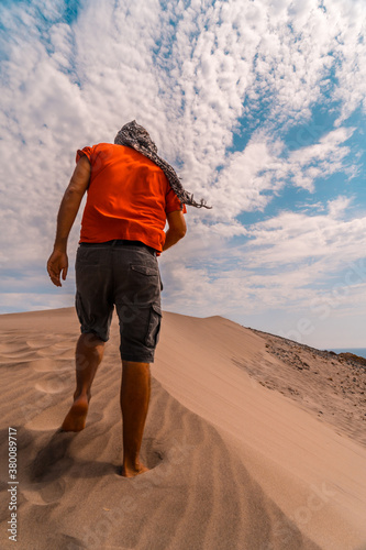 A man with a red shirt and a turban on his head  walking in the desert of the dune of Playa de M  nsul in the natural park of Cabo de Gata  Nijar  Andalucia. Spain  Mediterranean Sea