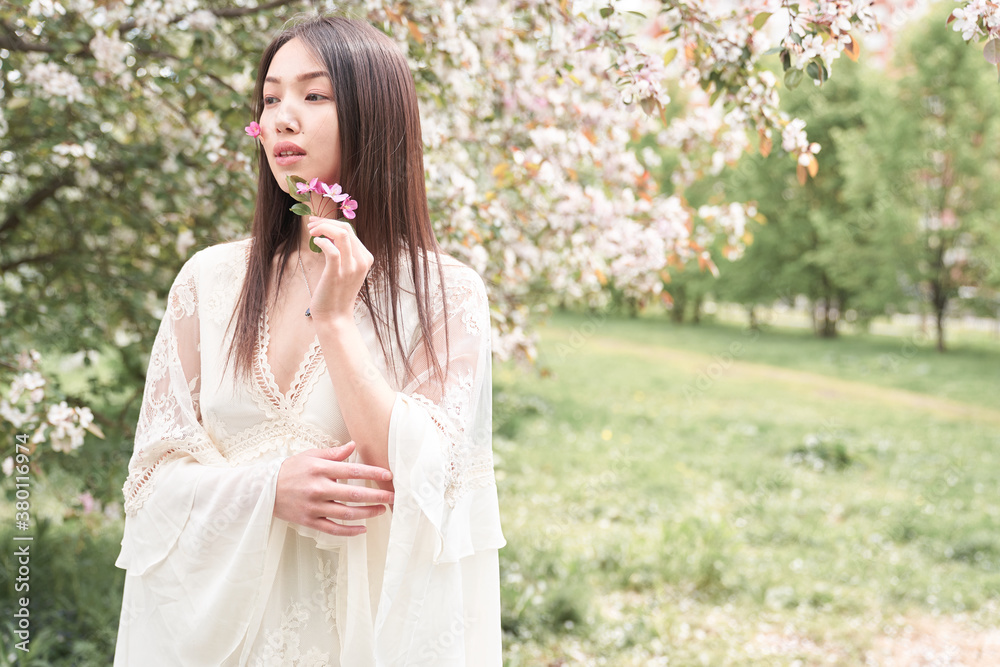 Portrait of a beautiful Asian woman in a white dress, she is standing near a tree with white flowers, on her cheeks flowers with petals are glued on a band-aid, she looks away Portrait of a beautiful Asian woman in a white dress, she is standing near a tree with white flowers, on her cheeks flowers with petals are glued on a band-aid, she looks away