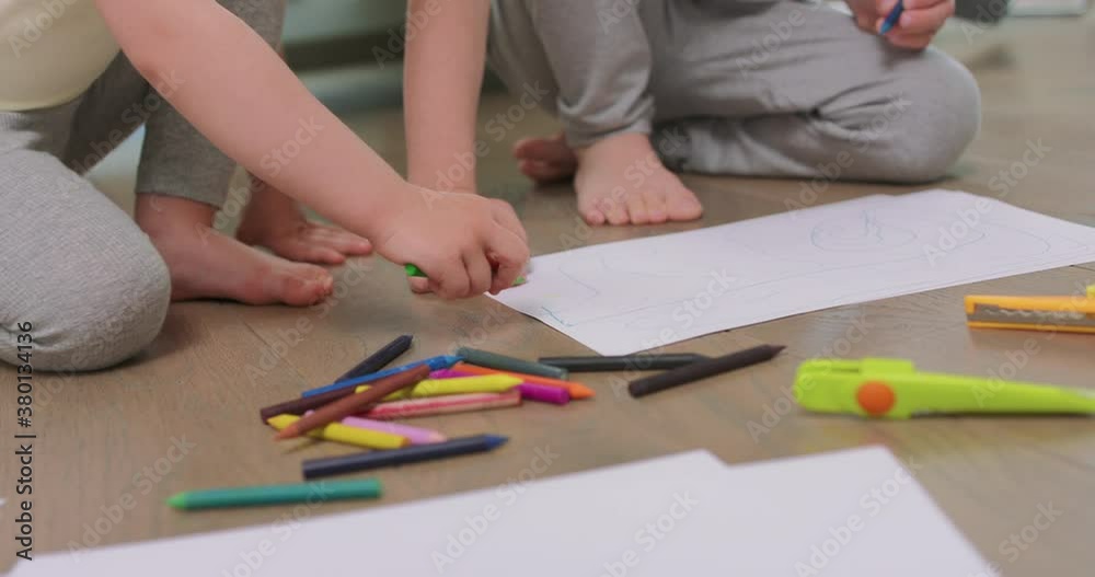 Close up o hands and feet of a little boy and a little girl, who are drawing with pencils on the white paper on the floor. Pencils, paper, kid's scissors and paper knives are in front of them. Close up o hands and feet of a little boy and a little girl, who are drawing with pencils on the white paper on the floor. Pencils, paper, kid's scissors and paper knives are in front of them.