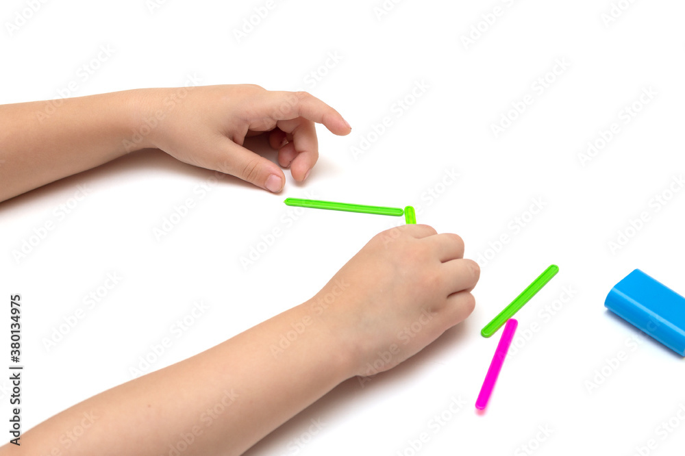 Child in kindergarten, school plays with counting sticks, learn to count, play, children's hands lay out figures from multi-colored sticks Isolated on white background Child in kindergarten, school plays with counting sticks, learn to count, play, children's hands lay out figures from multi-colored sticks Isolated on white background
