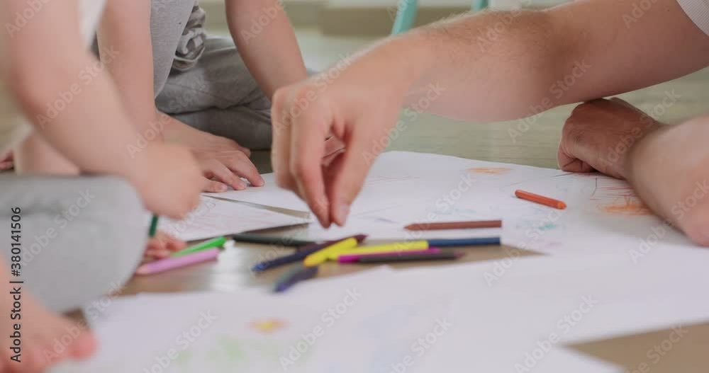 Close up of a little boy and a little girl, and their father are drawing with pencils on the white paper on the floor Close up of a little boy and a little girl, and their father are drawing with pencils on the white paper on the floor