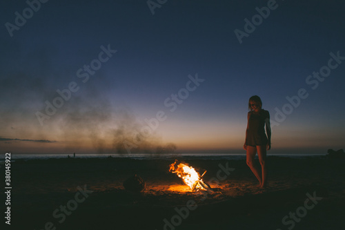 Woman enjoying the warmth of a bonfire on the beach under the stars.