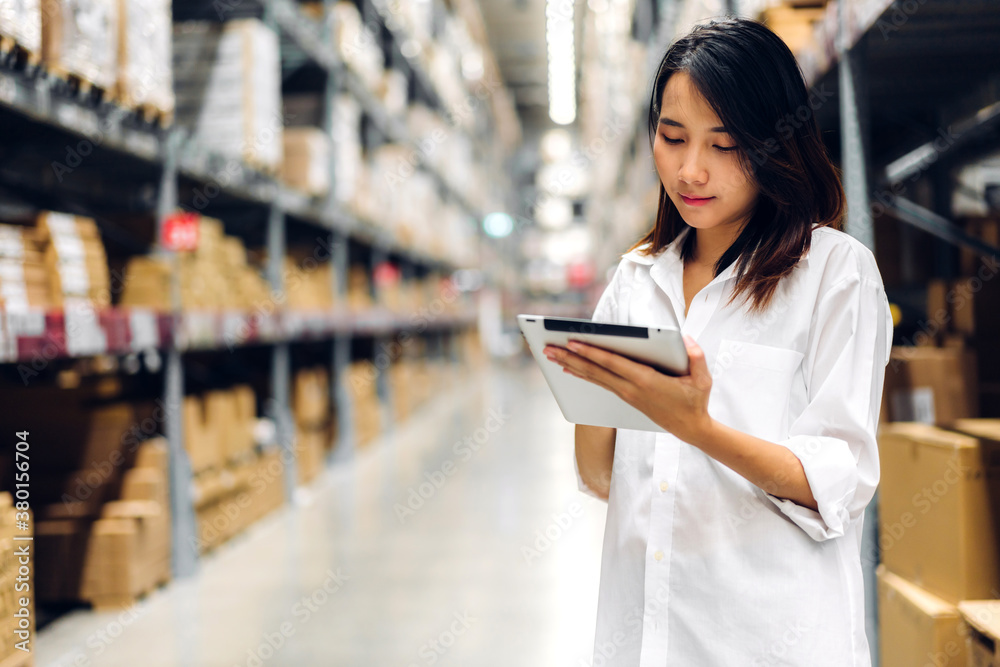 Portrait of smiling asian manager worker woman standing and order details on tablet computer for checking goods and supplies on shelves with goods background in warehouse.logistic and business export Portrait of smiling asian manager worker woman standing and order details on tablet computer for checking goods and supplies on shelves with goods background in warehouse.logistic and business export