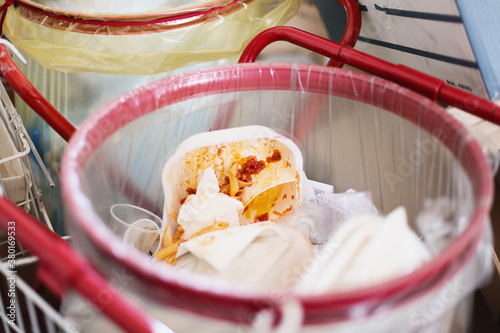Dirty disposable dishes and glasses in trash bin with some pasta