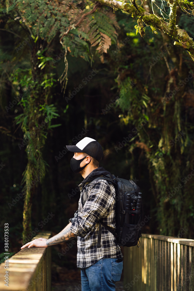 Young man wearing face mask and standing in the middle of a bridge during a trip. Tourism and Covid-19 concept Young man wearing face mask and standing in the middle of a bridge during a trip. Tourism and Covid-19 concept