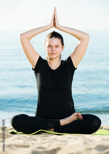 Fitness woman in black T-shirt is sitting and practicing yoga on nature.