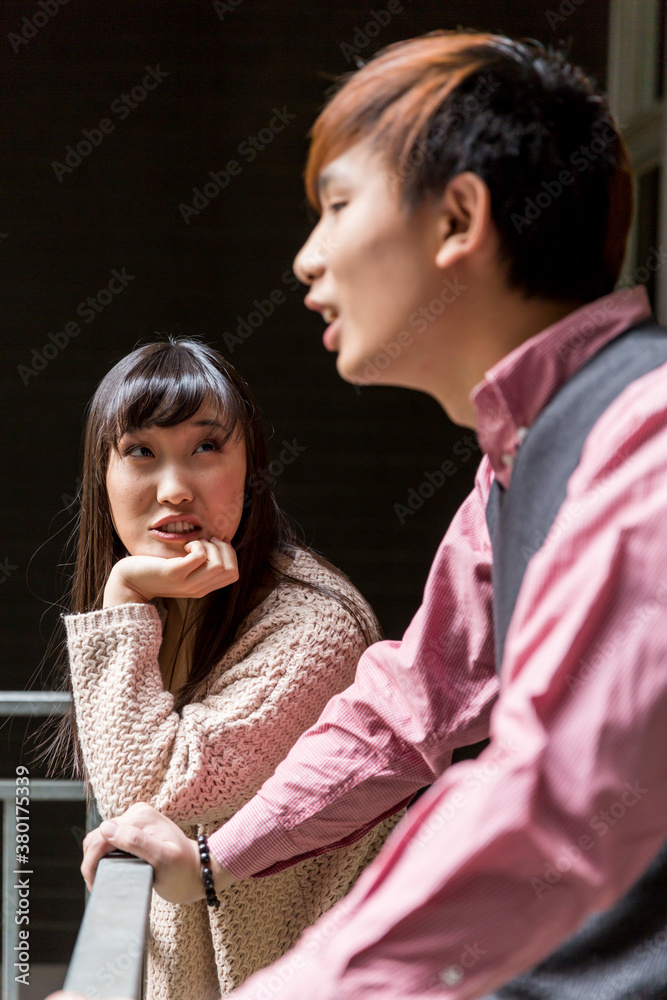 Young chinese couple standing on exteior balcony talking Young chinese couple standing on exteior balcony talking
