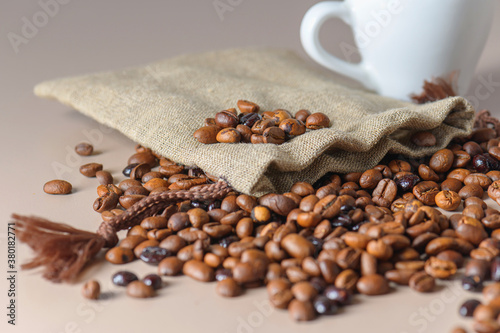 Roasted coffee beans, a white Cup, and a small burlap bag in close-up. Roasted coffee beans of the morning mood.