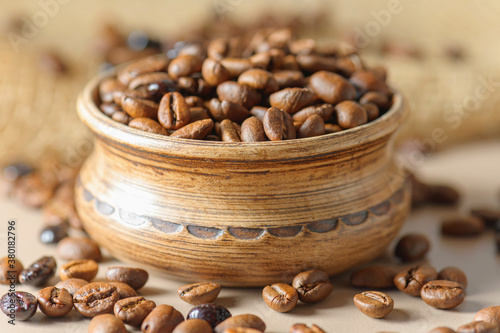 A pot of coffee beans on a sacking. Roasted coffee beans are scattered on the table. A mix of different types of coffee roasting.