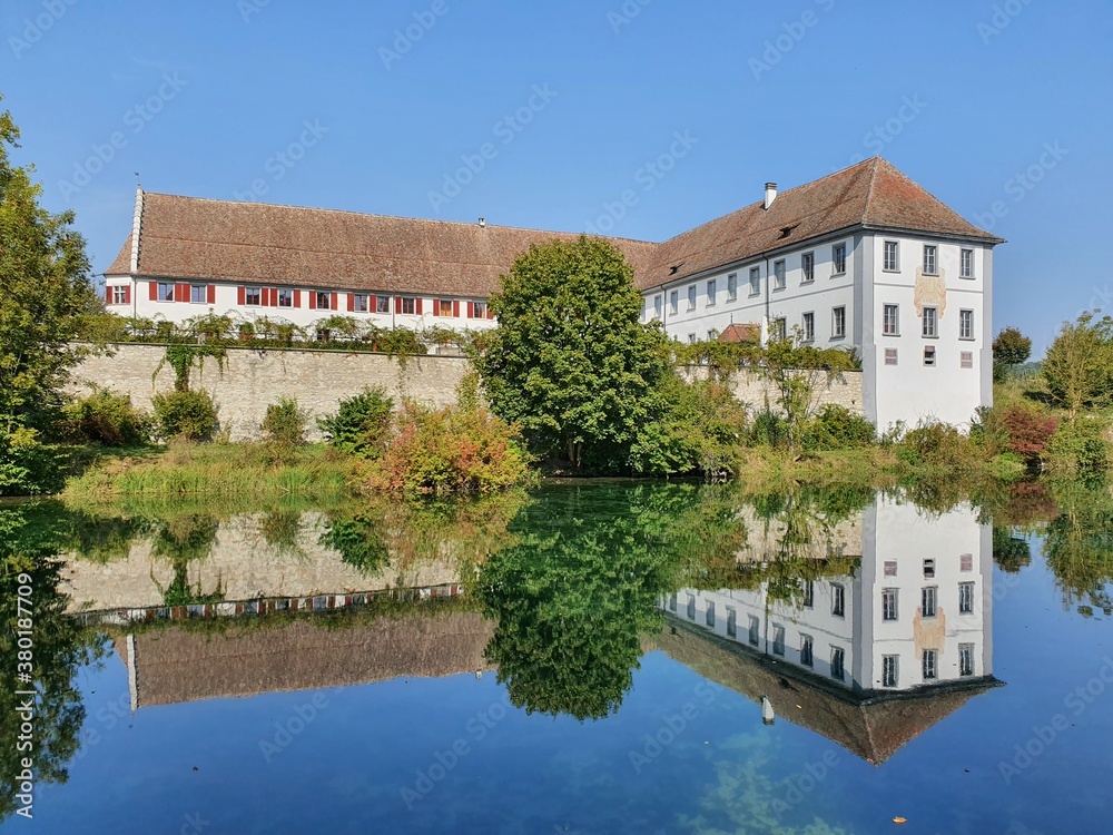 Kloster welches sich im Wasser spiegelt mit Fluss im Vordergrund