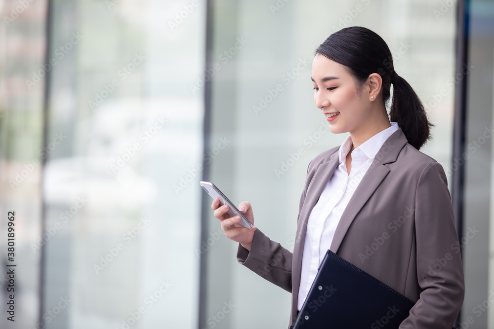 Asian woman with smartphone standing against street blurred building background, Fashion business photo of beautiful girl in casual suite with smart phone. 