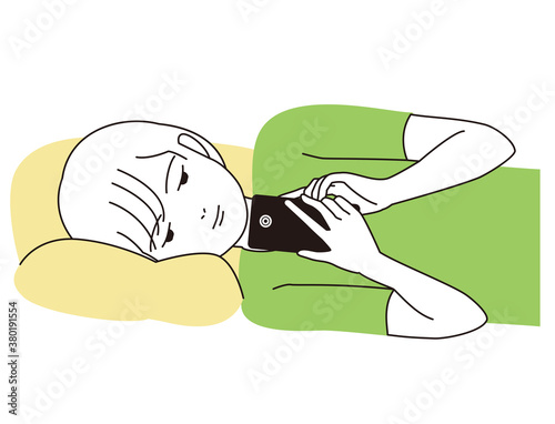 スマートフォンを寝転がってで見つめる男の子