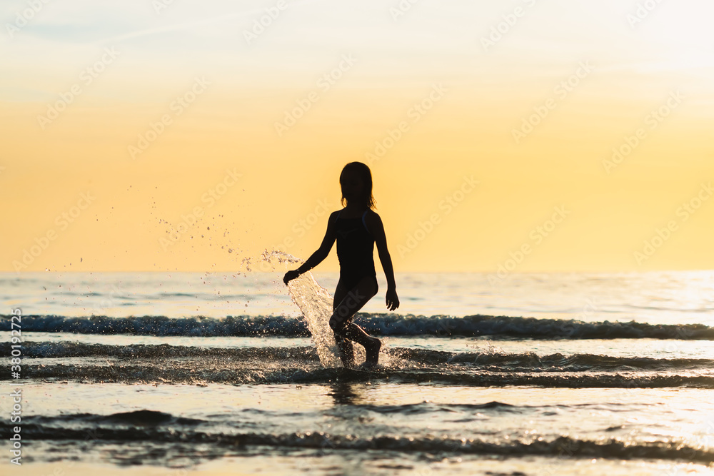 Silhouette of a little girl running in the ocean at sunset Silhouette of a little girl running in the ocean at sunset