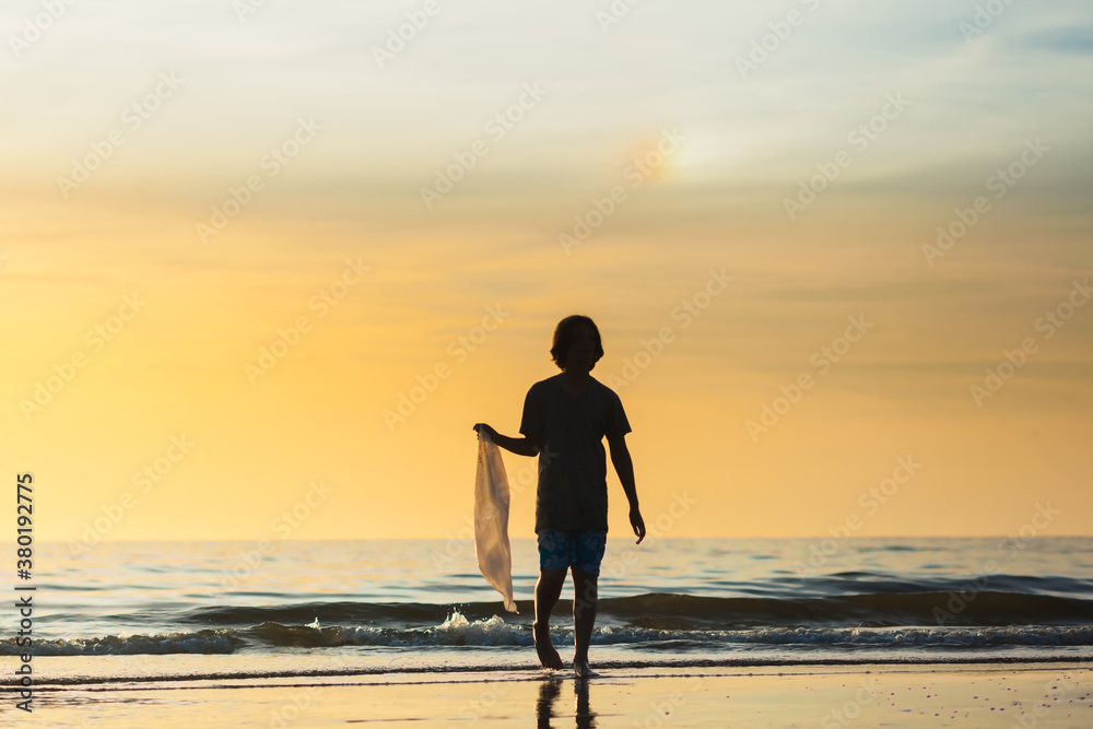 Silhouette of a boy getting a plastic bag out of the ocean at sunset Silhouette of a boy getting a plastic bag out of the ocean at sunset
