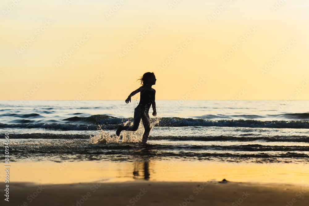 Silhouette of a little girl running along the shoreline at sunset Silhouette of a little girl running along the shoreline at sunset
