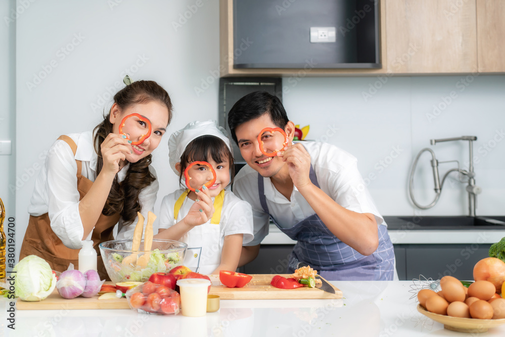 Asian family with father, mother and cute little girl daughter in chef's hats are having fun while cooking in kitchen at home. Asian family with father, mother and cute little girl daughter in chef's hats are having fun while cooking in kitchen at home.