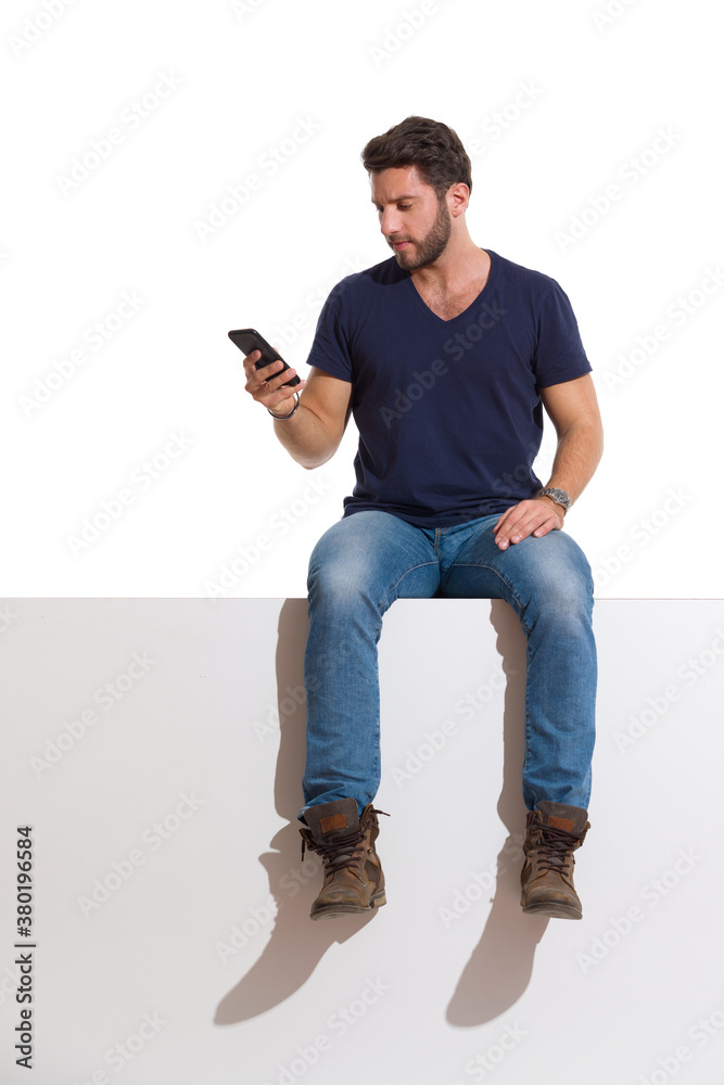 Handsome Man Is Sitting Relaxed On A Top, Holding Telephone And Reading Handsome Man Is Sitting Relaxed On A Top, Holding Telephone And Reading