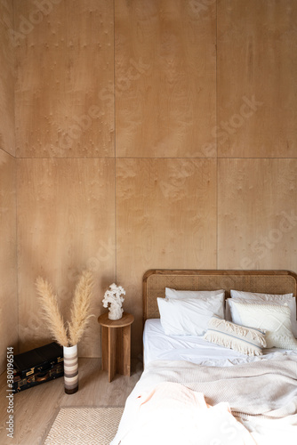 Stylish Bedroom corner with rattan headboard and bed with soft pillows setting with white pillows plywood wall on the background / cozy interior design / modern interior