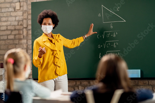 Obraz na plátně Black teacher wearing face mask while explaining math lesson in the classroom