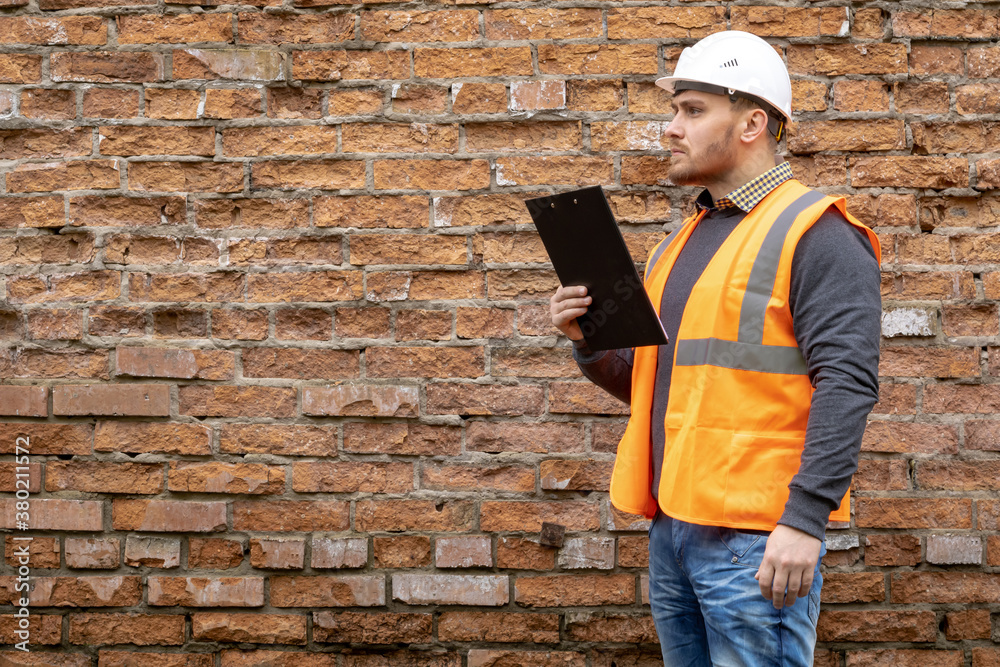 Builder in a hard hat on a brick wall background. Builder in a hard hat on a brick wall background.