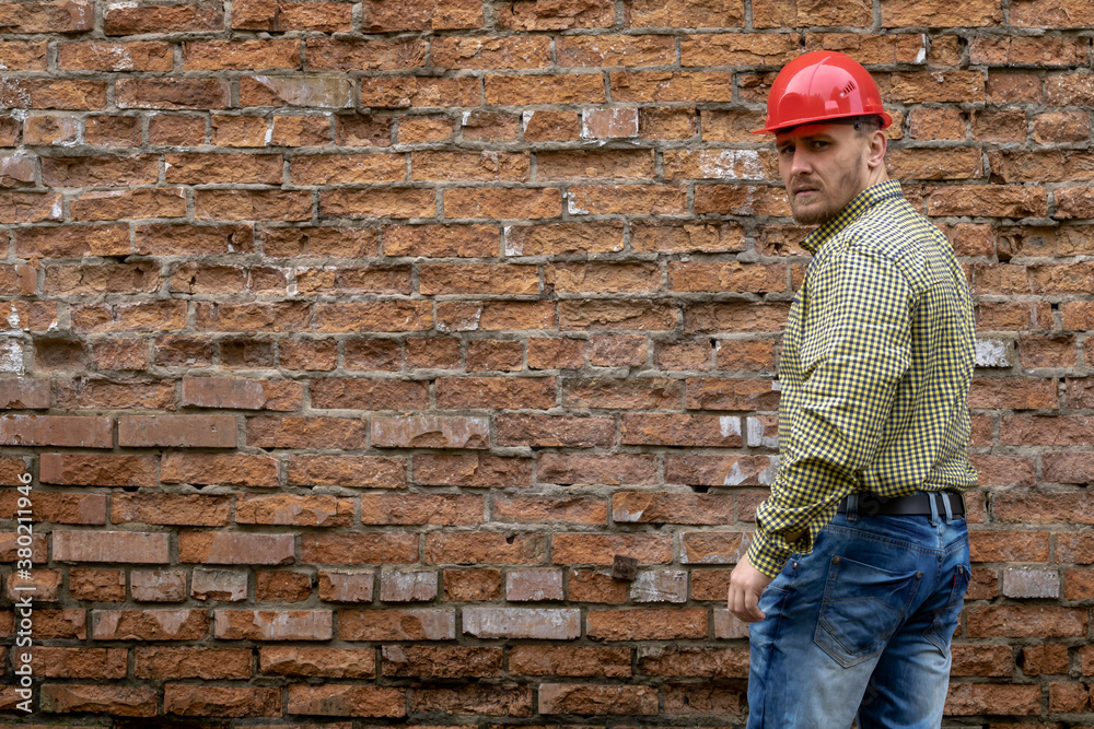Builder in a hard hat on a brick wall background.