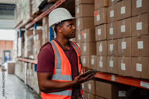 Concentrated factory worker holding digital tablet locating parcels for delivery standing in warehouse