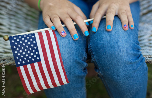 Teen girl in jeans with patriotic nails and holding a flag