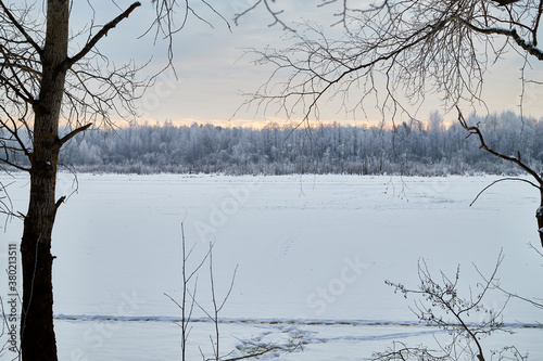 View from the shore of a river or lake, when the water is covered with a of ice powdered with snow and trees foreground. Winter landscape photo