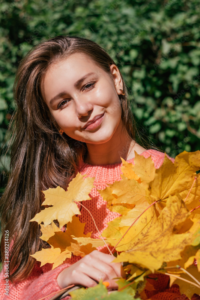 Portrait of a beautiful teenage brunette girl with yellow maple leaf. Autumn concept.
