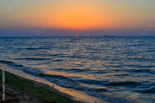 bright red circle of sun yellow pink orange dawn at sea coast  sand shore with waves