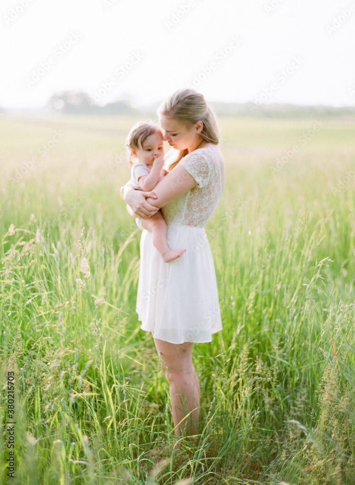Mother holding and embracing her young daughter in a wide open field of grass Mother holding and embracing her young daughter in a wide open field of grass