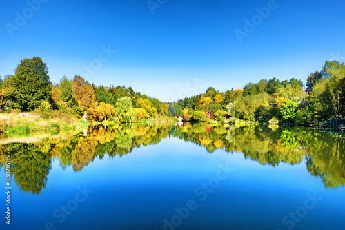 golden autumn countryside landscape against blue sky background. Colorful forest reflection on pond water. Orange red yellow and green foliage. Autumn in park. Russian nature. Rural landscape