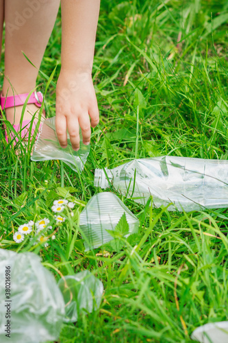 Hand of child cleans green grass from plastic trash in the park