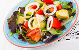 Image of salad with arugula, tomato and avocado on the plate indoors.