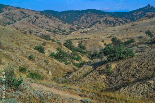 View of green mountain range with small peaks, Crimea. Serene picturesque green valley, hills. Scenery of nature. Yellow dry grass, bushes, green trees.