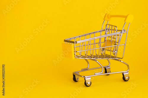 Mini shopping cart isolated on yellow background. Empty supermarket trolley. Buying online concept. Copy space
