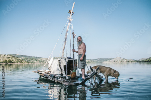 stranded old man on a handmade wooden raft with his dog photo