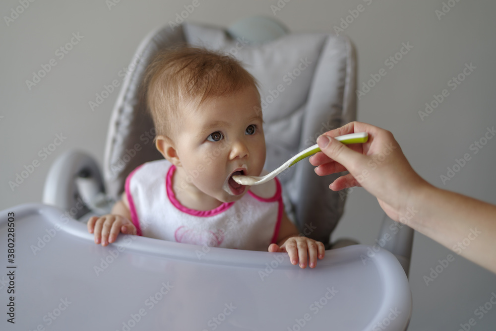 Baby girl in high chair eating her baby food Baby girl in high chair eating her baby food