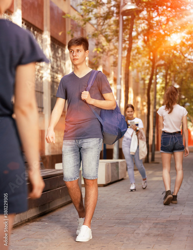 Full length portrait of modern teenager dressed in blue tee shirt and denim shorts walking along city street on summer day