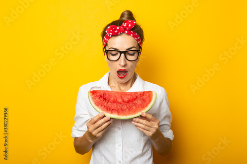 Young woman with a smile in a red headband and glasses eats watermelon on a yellow background