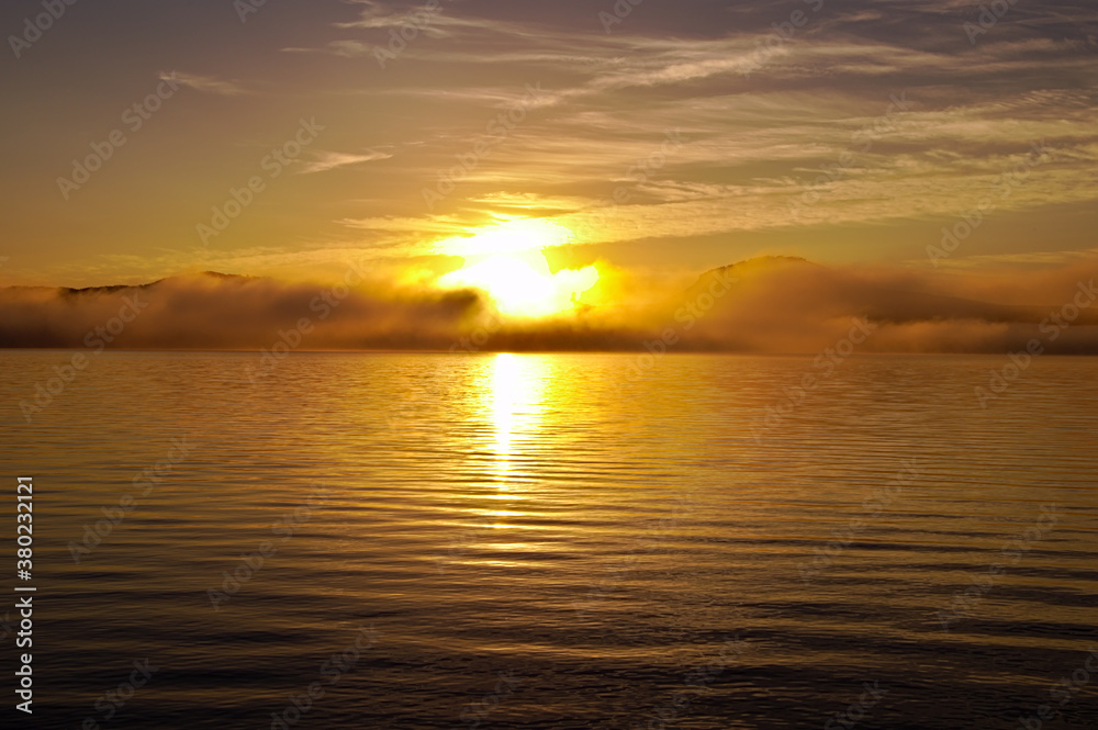 湖面に雲の漂う早朝の湖に昇る朝日