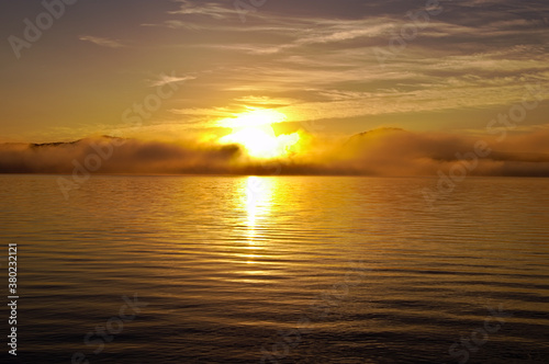 湖面に雲の漂う早朝の湖に昇る朝日